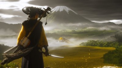 Ghost of Yotei screenshot showing the protagonist looking over a field of golden grasses, a snow covered mountain is in the distance